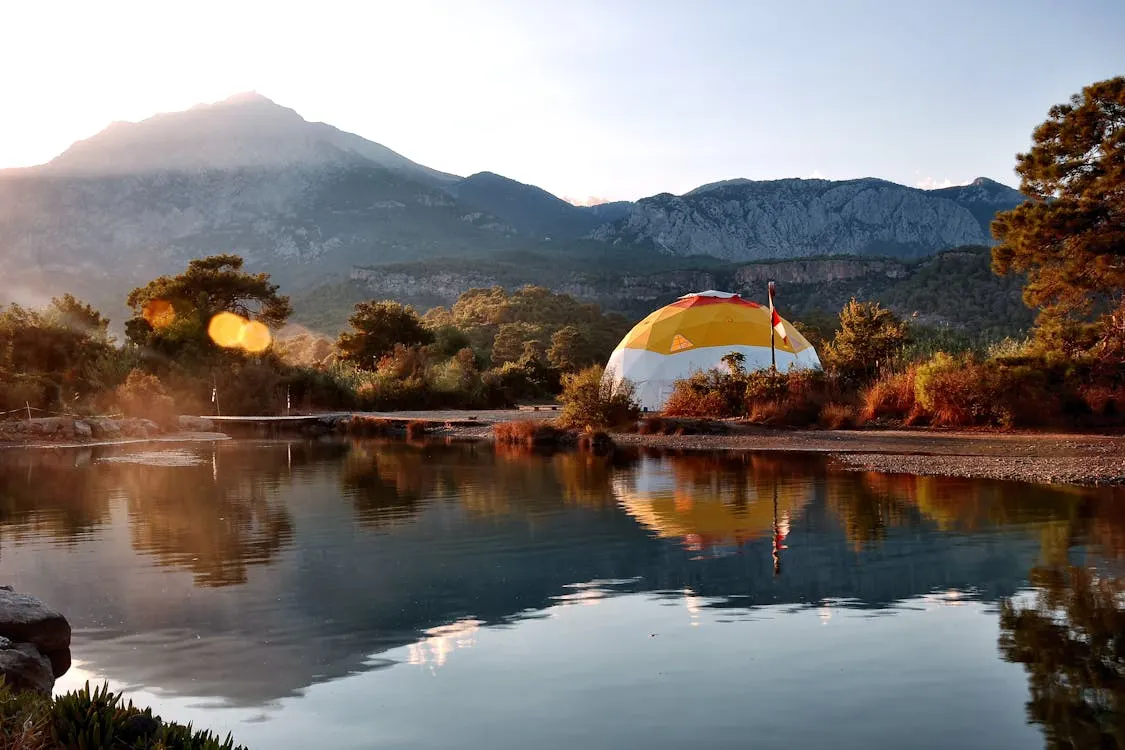 Dôme insolite illuminé au bord d'un lac, entouré de montagnes au lever du soleil