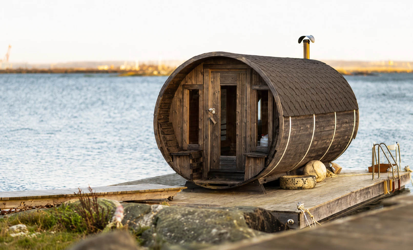 Cabane tonneau en bois installée sur un ponton au bord de l'eau, au coucher du soleil